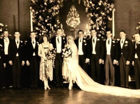 A vintage wedding photo featuring a bride and groom surrounded by their wedding party in formal attire