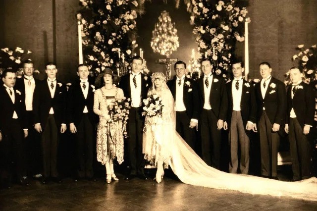 A vintage wedding photo featuring a bride and groom surrounded by their wedding party in formal attire