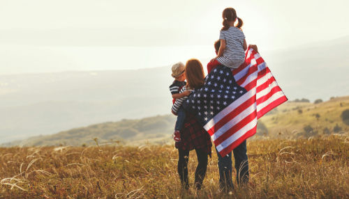 Family holding American flag in a field.