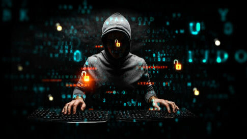Hooded hacker using two keyboards surrounded by code.