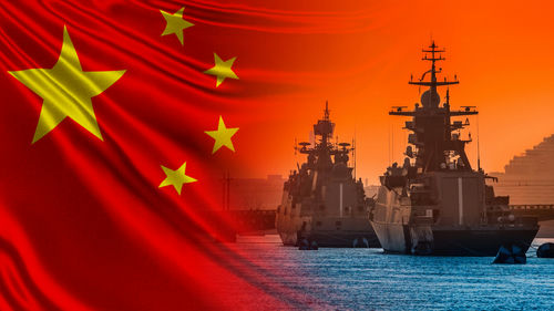 Chinese flag overlaying naval ships at sunset.