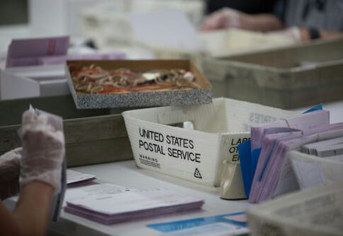 USPS worker handling mail-in ballots at a sorting facility.