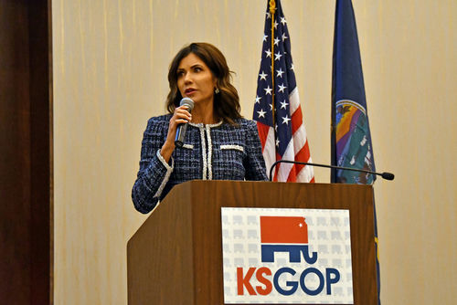 Woman speaking at podium with KS GOP logo and flags.