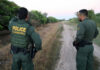 Two U.S. Border Patrol officers standing on a dirt path.