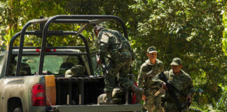 Soldiers loading equipment into a military vehicle in forest.