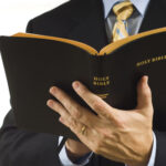 Man in suit holding an open Holy Bible.