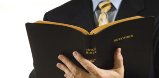 Man in suit holding an open Holy Bible.
