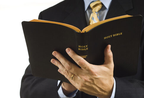 Man in suit holding an open Holy Bible.