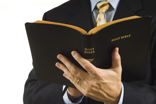 shutterstock_10073746.jpg featured image Man in suit holding an open Holy Bible.