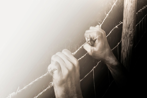 shutterstock_1085068871.jpg featured image Hands gripping barbed wire fence.