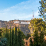Hollywood Sign on hillside surrounded by trees, clear sky.