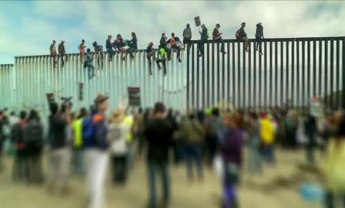 shutterstock_1229072281.jpg featured image Crowd and people climbing large border wall during protest.