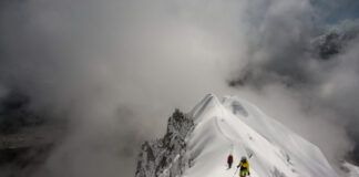 Climbers ascending a snowy mountain ridge under a cloudy sky