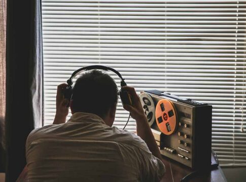 Person wearing headphones listening to a reel-to-reel tape recorder