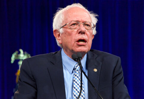 Bernie Sanders speaking at an event, wearing a suit.