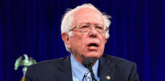 Bernie Sanders speaking at an event, wearing a suit.