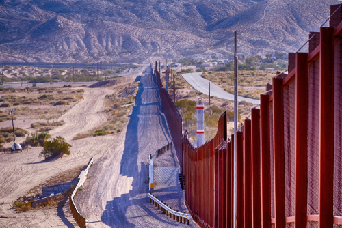 Border wall stretching through desert landscape with mountains.