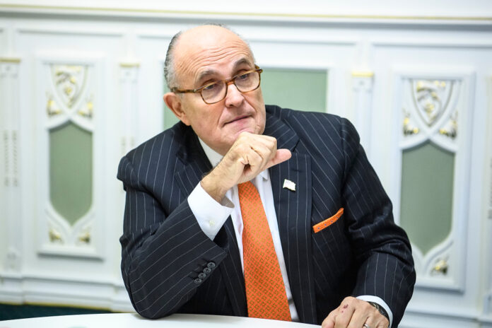 shutterstock_1566583993 featured image Rudy Giuliani Man in suit sitting at a table indoors