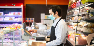 Man in mask and apron working at deli counter.