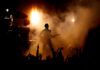Guitarist performing on stage with crowd and bright lights.