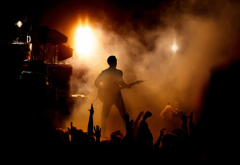 Guitarist performing on stage with crowd and bright lights.
