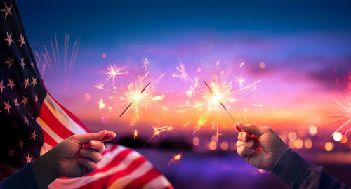 Hands holding sparklers with American flag background.