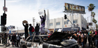 Protesters standing on damaged police car, holding signs.