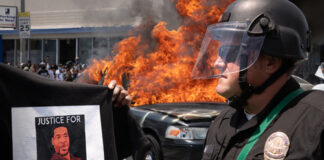 Protester with George Floyd shirt, police officer, burning vehicle.