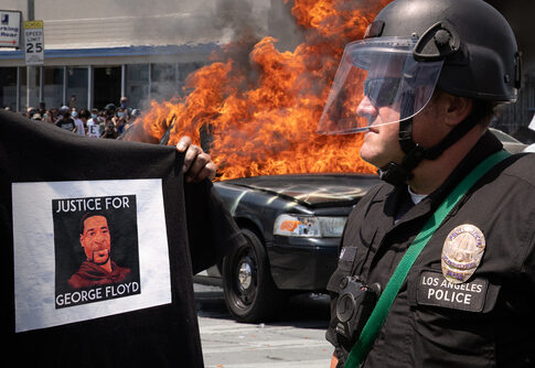 Protester with George Floyd shirt, police officer, burning vehicle.