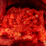 Open bag of red, spicy cheese puff snacks.