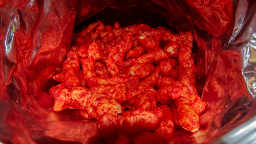 Open bag of red, spicy cheese puff snacks.