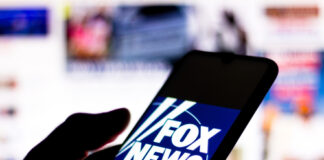 Silhouette hand holding phone displaying Fox News logo.