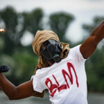 Person in gas mask with Molotov cocktail, shirt.