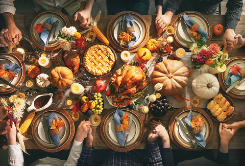 shutterstock_1820787251.jpg featured image Thanksgiving feast with people holding hands around table.