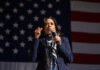 A person speaking in front of an American flag.