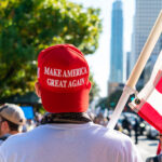 Person in MAGA hat holding U.S. flag at rally.