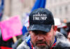 Man wearing God Guns Trump hat in a crowd.