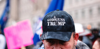Man wearing God Guns Trump hat in a crowd.