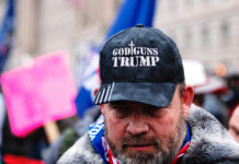 Man wearing God Guns Trump hat in a crowd.