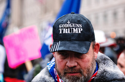 Man wearing God Guns Trump hat in a crowd.