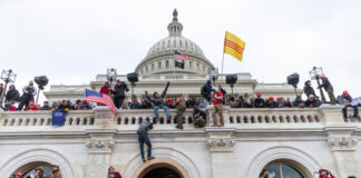 Crowd at U.S. Capitol building with flags and cameras.
