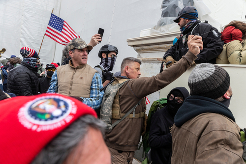 shutterstock_1889190946.jpg featured image People at U.S. Capitol riot, holding flags and phones.