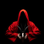 Hooded figure in red cloak holding a goat skull.