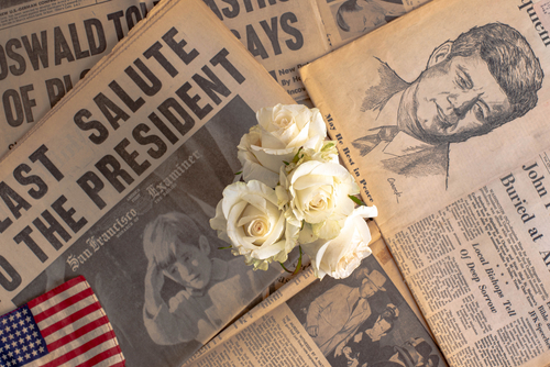 Newspapers about John F. Kennedy, white roses on top.