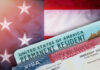 Green card and visa with U.S. flag background.