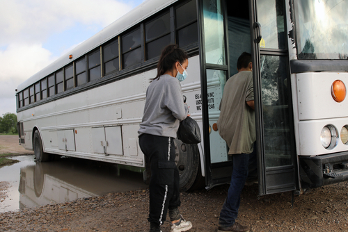 shutterstock_1992714503.jpg featured image People boarding a white bus on a dirt road.