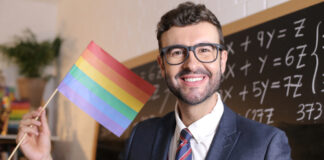 Man holding rainbow flag in classroom.