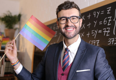 Man holding rainbow flag in classroom.