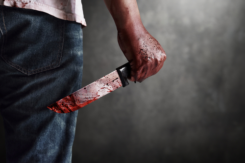 shutterstock_2025646316.jpg featured image Person holding bloodstained knife behind back.