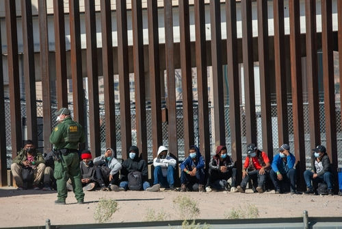 shutterstock_2079408463 (1).jpg Border patrol agent with group of seated immigrants.
